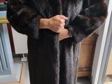 man in a fur coat standing in a kitchen next to a window