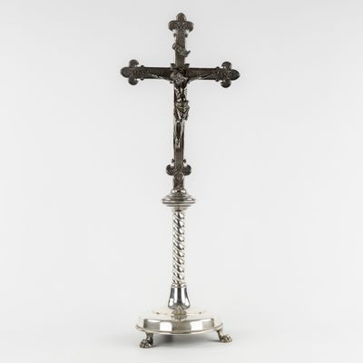 a silver cross on a pedestal with a white background