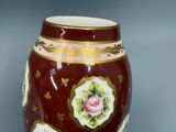 un vase rouge orné d'une bordure dorée et d'une rose rose