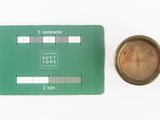 a small coin next to a green card on a white surface