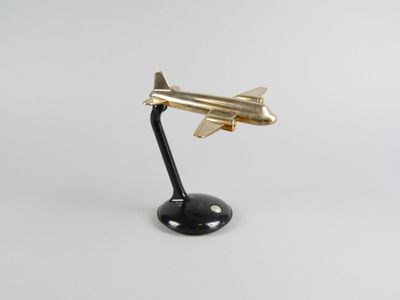 un petit avion doré posé sur un socle noir, sur une surface blanche