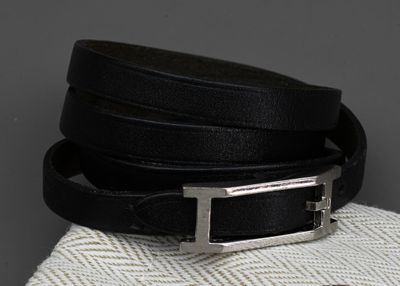 une ceinture en cuir noir avec une boucle argentée, posée sur un tissu blanc