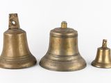 three antique brass bells sitting next to each other on a white surface
