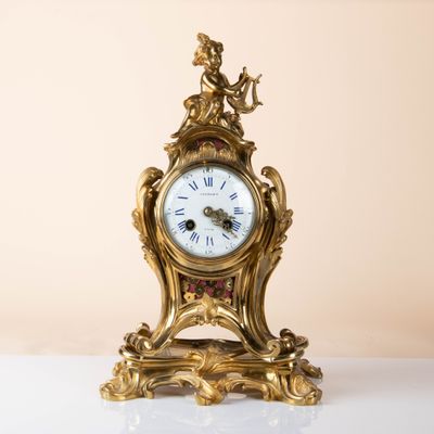 a gold clock on a white table with a beige background