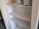 a white shelf in the corner of a room with a coffee pot on top of it