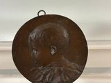 an antique bronze plaque of a boy with a bow on his head