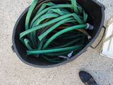 a bucket full of green hoses next to a person ' s feet