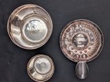 two silver dishes and a spoon on a black surface