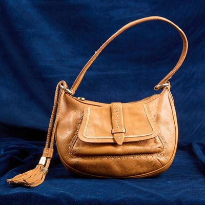 sac à main en cuir beige avec des pompons sur fond bleu