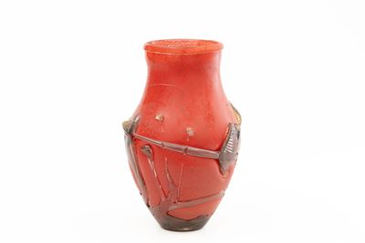 un vase rouge orné d'un oiseau, posé sur un fond blanc