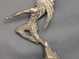 statue of a man on a surfboard holding a bell on a gray surface