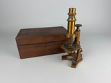 un microscope ancien en laiton avec son coffret en bois, sur fond blanc
