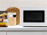a microwave sitting on a white counter top with a magazine on it