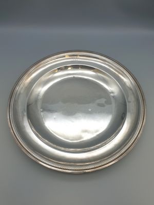 une assiette en argent posée sur une table blanche, sur fond noir