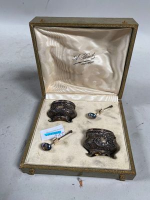 deux objets en métal argenté dans un coffret doré posé sur une surface blanche