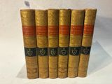 five old books are lined up in a row on a white surface