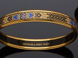 two gold and blue enamel bang bracelets on a black surface