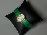 un oreiller noir orné d'une bande verte et sur lequel repose une montre blanche
