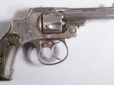 un revolver argenté posé sur une surface blanche, avec un fond blanc