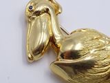 gold plated pelican brooch with blue eyes on white surface