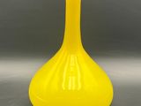 yellow glass vase sitting on top of a table on a gray surface
