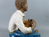 a figurine of a boy with a bowl on his lap