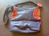 un sac à main violet et orange posé sur la table, à côté d'un téléphone portable