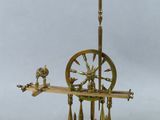 une machine à filer ancienne en laiton, posée sur un socle surmonté d'une horloge
