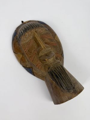 un vieux masque en bois posé sur une surface blanche, avec un fond blanc