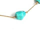 a close up of a necklace with turquoise stones on a white surface