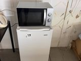 un micro-ondes posé sur un petit réfrigérateur, à côté d'une table