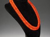 an orange beaded necklace is displayed on a black mannequin