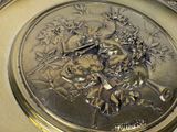 a silver clock with a picture of a woman and a bird on it