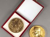 une image représentant une médaille d'or dans un coffret rouge, à côté d'une pièce d'or
