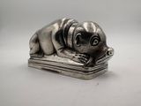 a silver figurine of a dog laying on top of a book