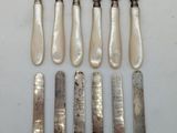 eight silverplated knives and a knife holder on a white surface