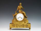 a gold clock with a woman sitting on top of it