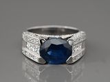 une bague sertie d'un saphir bleu et de diamants posée sur une surface réfléchissante