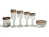 six verres à vin à bord doré sont alignés sur une surface blanche