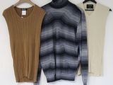three sweaters hanging on a wooden hanger in front of a white wall