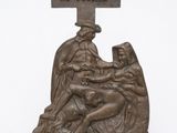 statue en bronze représentant une femme agenouillée sur une croix, aux côtés d'un homme tenant un bébé dans ses bras
