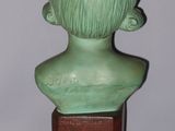 a green bust of a young boy on a wooden stand