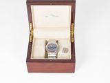 une photo d'une montre dans un coffret en bois posée sur une surface blanche
