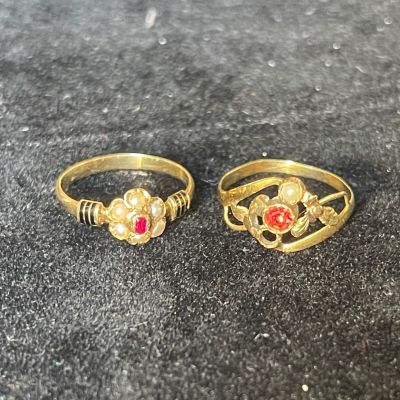 two gold rings with red stones on them sitting on a black surface