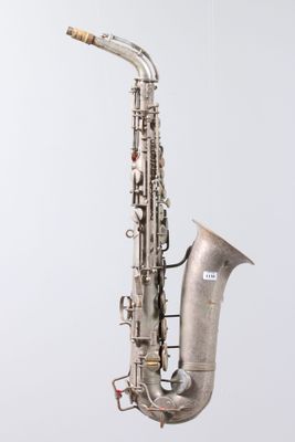 an old silver saxophone hanging from a string on a white wall