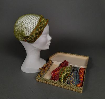 une tête de mannequin blanche coiffée d'un chapeau vert et accompagnée d'une boîte de cravates