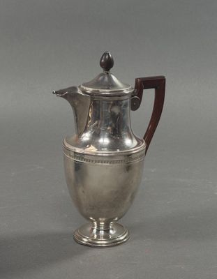une cafetière ancienne en argent, dotée d'une poignée en bois sur un fond gris