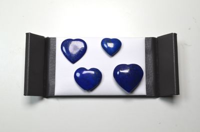 quatre boutons bleus en forme de cœur dans une boîte noire posée sur une surface blanche