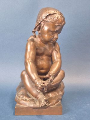 statue en bronze représentant un garçon assis sur un rocher, les mains posées sur les genoux