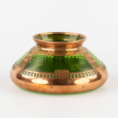 un vase en verre vert bordé d'or, posé sur un fond blanc